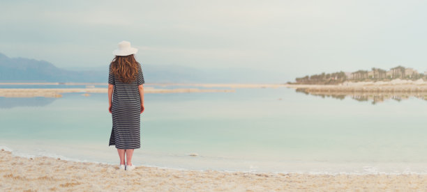 在死海海滩附近穿着水手条纹衣服的女人。旅游、暑假、假期、自由理念。数字排毒。海背景与复制空间。横幅。图片下载
