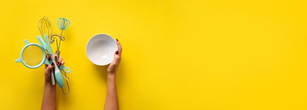 黄色背景上的女人手里拿着厨房用具。烘烤工具-碗，刷子，搅拌器，抹刀。烘焙、烹饪、健康自制食品的概念。本空间图片下载