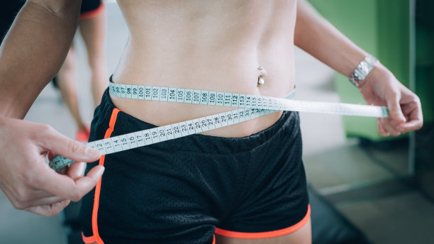 一位身材匀称的妇女正在用卷尺量她的腰围图片下载