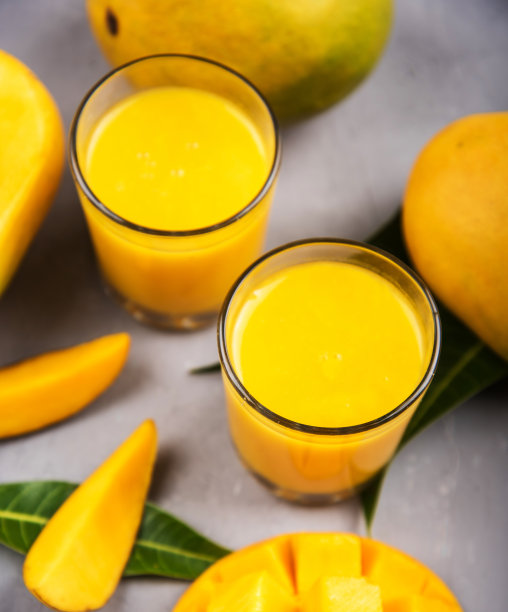 近距离的芒果冰沙在一个玻璃杯和芒果片上的桌子图片下载
