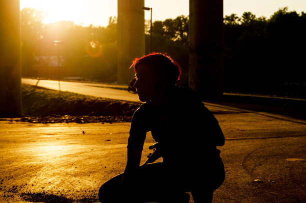 年轻女子的剪影跪在城市街道在夕阳的黄金时间图片下载