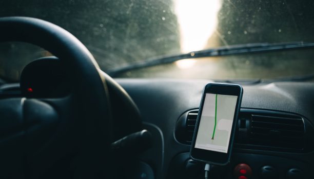 用智能手机上的导航仪开车。司机的手放在方向盘上。图片下载