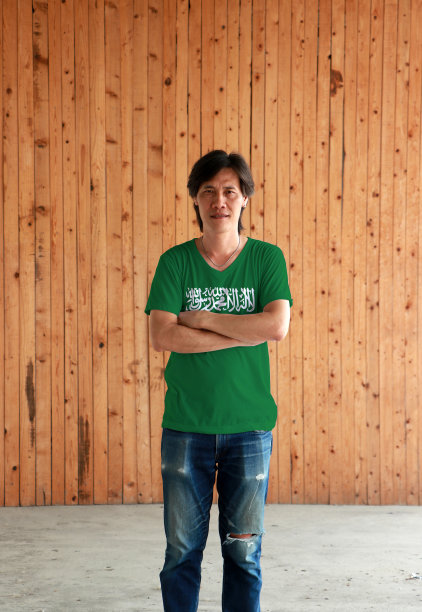穿着沙特阿拉伯国旗颜色衬衫的男人，在木墙背景前交叉双臂图片下载
