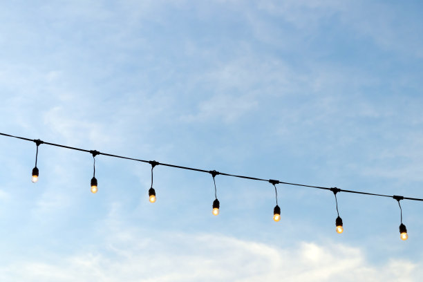 用线串起的灯泡和蓝天上蓬松的云朵。图片下载