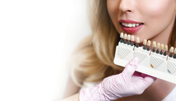 洁白的牙齿和美丽的微笑，一个年轻女子。使用阴影指南来匹配种植体的阴影。牙科诊所牙齿美白的准备工作。特写微距白色背景孤立图片下载