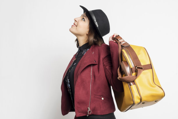 侧面的时尚女人休闲服装站着，同时拿着一个手提包对白色的背景图片下载