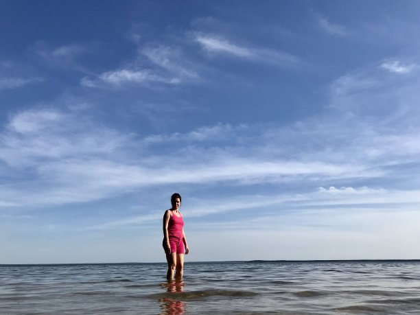 这个女孩在湖岸边的浅水中走过。可见清澈的水和美丽的蓝天。图片下载