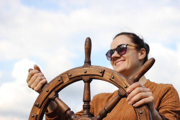 女孩控制着游艇，双手放在方向盘上，手轮在天空背景上图片下载