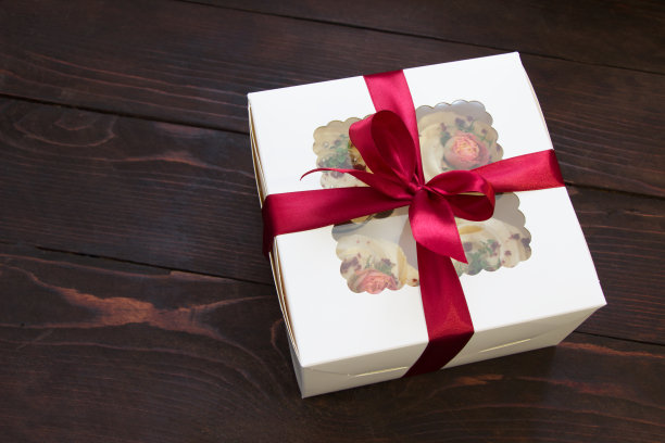 纸杯蛋糕礼盒。白色盒子与红色蝴蝶结在木板上。甜蜜的礼物图片下载