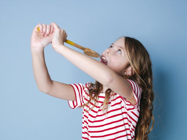 一个漂亮的小女孩用勺子当麦克风，在蓝色的背景下唱歌图片下载