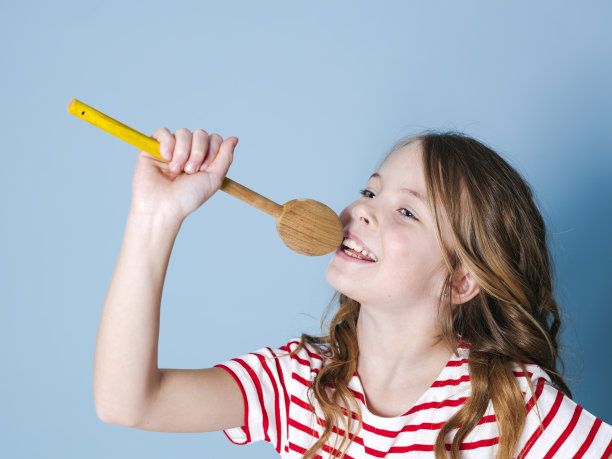 一个漂亮的小女孩用勺子当麦克风，在蓝色的背景下唱歌图片下载