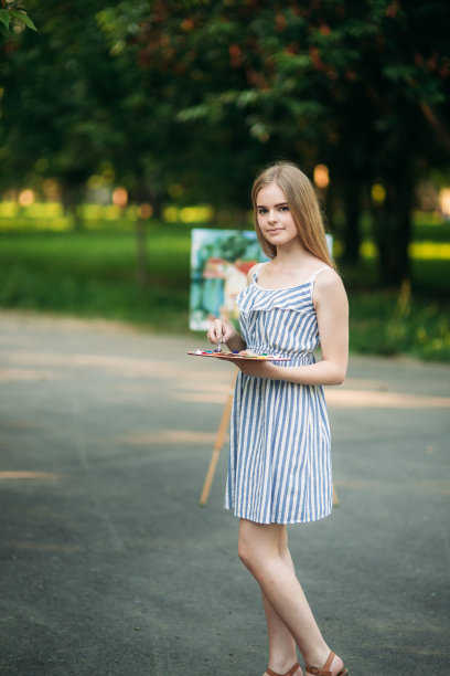 美丽的女孩在公园里用调色板、颜料和抹刀画画。一幅画的画架和帆布。的背景图片图片下载