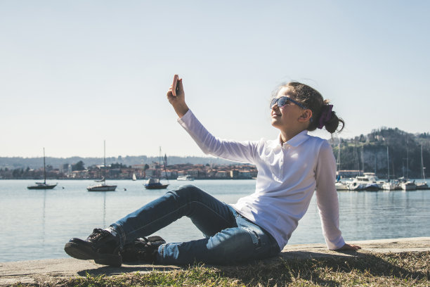 一个小女孩在和远方的朋友视频通话。无线技术有助于在任何地方保持联系。漂亮的孩子在湖边自拍。用智能手机自拍。孩子在网上聊天图片下载