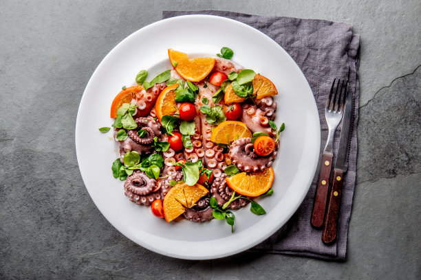 全章鱼沙拉配橙汁，西红柿和西洋菜沙拉放在白色盘子里。俯视图图片下载