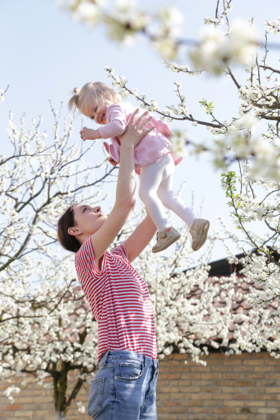 年轻快乐的妈妈抱着她可爱的宝贝女儿玩耍，偷拍户外照片，家庭生活理念图片下载