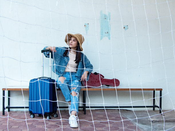 美丽的女人坐在木椅旁边的行李和尤克里里琴盒，准备旅行，度假图片下载