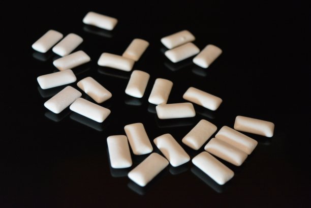 在黑色光滑的背景上，放着白色的口香糖枕头，用反射来保健和护理牙齿。图片下载