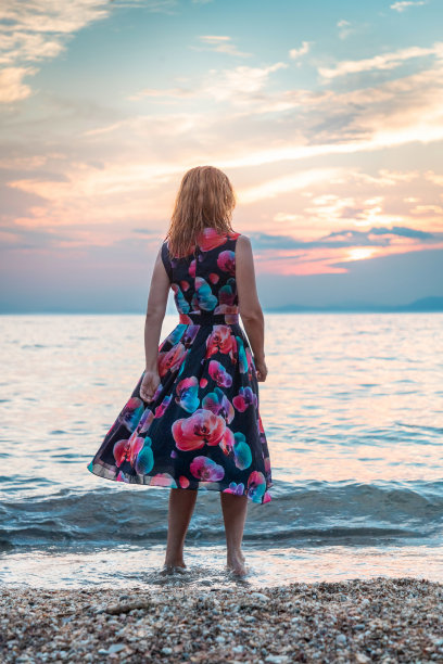 红发女人穿着衣服在海滩上看日落图片下载