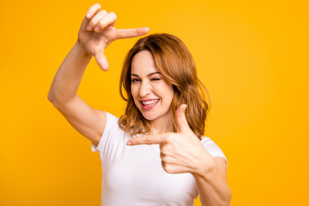 近距离的照片美丽的惊人的她，她的狐狸精女士大喜的手，手，手指，假装对焦摄影师创造性的思维，眨眼，穿着休闲的白色t恤孤立的黄色背景图片下载