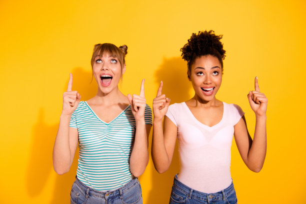 近距离的照片美丽的两个人，她，她的模特夫人多样性举起食指向上看空旷的空间，惊讶，奇怪穿休闲的白色条纹t恤，衣服孤立的黄色明亮的背景图片下载