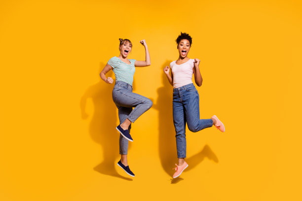 全身的长度，身体的大小，身材，视野，照片积极的，愉快的，内容的反应，学生女士，举起拳头，尖叫，叫喊，是的，幸运的，幸运的，瞄准，波浪卷曲的，顶结的，时髦的t恤，牛仔裤，孤立的黄色背景图片下载