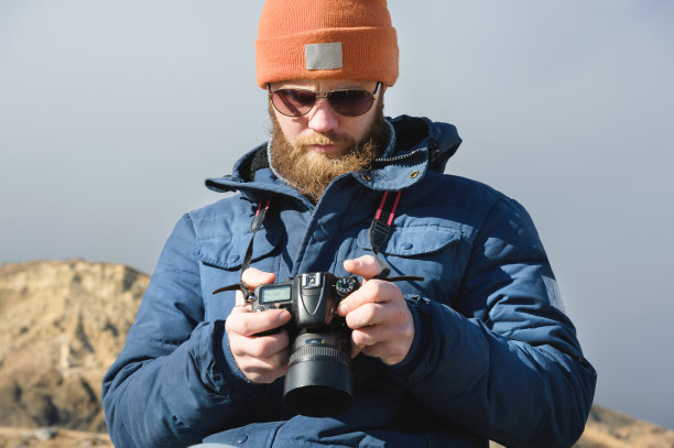 近距离肖像胡子男性摄影师戴着太阳镜，手里拿着单反相机看着相机上的照片图片下载