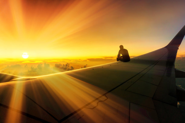 冒险旅行概念照片剪影的人坐在飞机机翼上看惊人的日落世界目的地图片下载