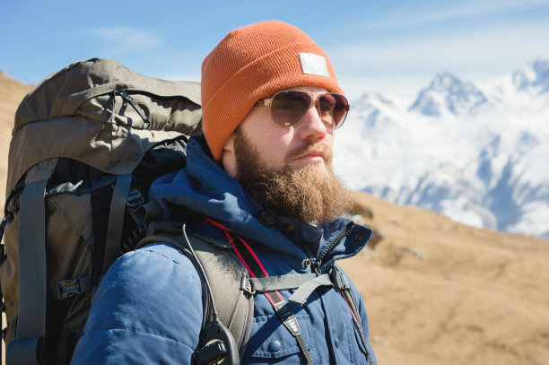 一个戴着太阳镜，穿着暖和的夹克，背着背包的大胡子男人的特写图片下载