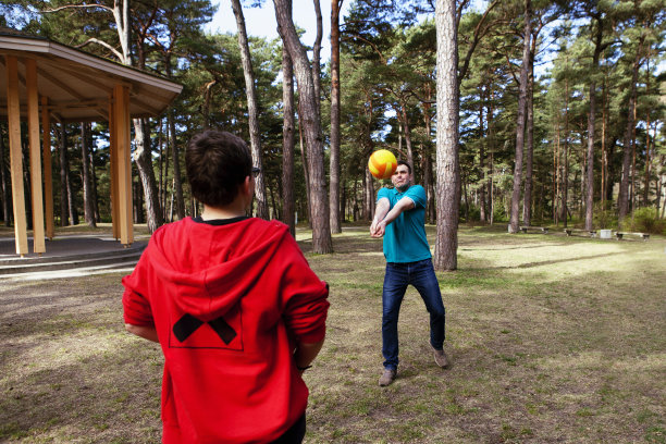 一位英俊的父亲和他的儿子在一个美丽的松树公园里打排球。图片下载