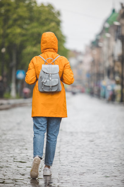 穿着黄色雨衣的女人在雨中走在城市的街道上图片下载