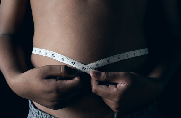 胖小子拿着卷尺在黑色的背景上检查身体，注意健康的概念。图片下载