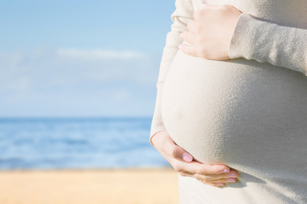 孕妇站在海滩上。阳光明媚的一天。情感爱怀孕的时间。孩子的期望。为可爱的，鼓舞人心的文字，积极的引用或可爱的语录空的地方。大肚皮特写镜头。图片下载