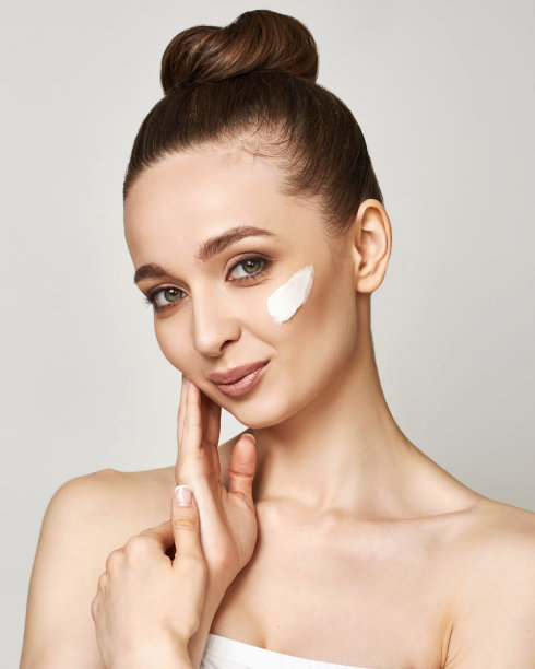 年轻女子在脸上擦面霜。护肤和化妆品的概念。自然妆容，触感十足。图片下载