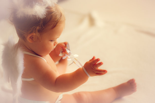 小女孩戴着天使的翅膀在床上玩耍图片下载