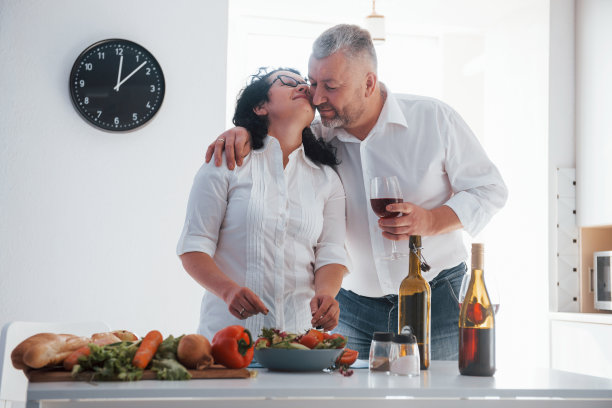 漂亮的照片。男人和他的妻子穿着白衬衫在厨房里用蔬菜做饭图片下载