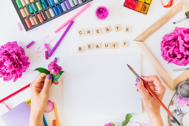 俯视图女性手握画笔在空白画布上创建美丽的字母，绘画材料和花在白色的背景。给你的生活增添色彩，让自己开朗上进，灵感迸发。图片下载