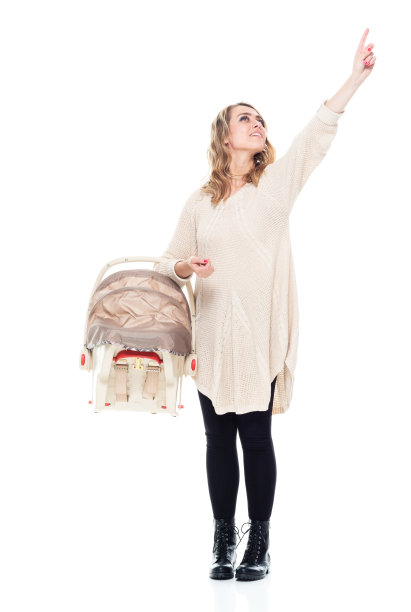 有吸引力的女人抱着一个婴儿汽车座椅和穿着暖和的衣服-前面的观点，指向和触摸图片下载