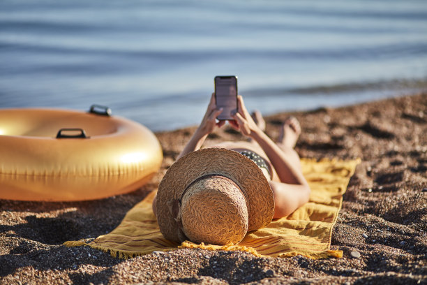 一个在海滩上玩智能手机的女人图片下载