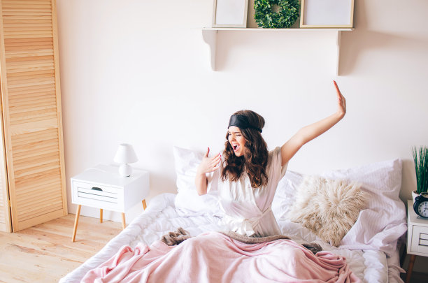 黑发美丽年轻的黑发姑娘在她的床上醒来。伸懒腰，打呵欠。独自在卧室。敷在额头上的睡眠面膜。早上醒来。图片下载