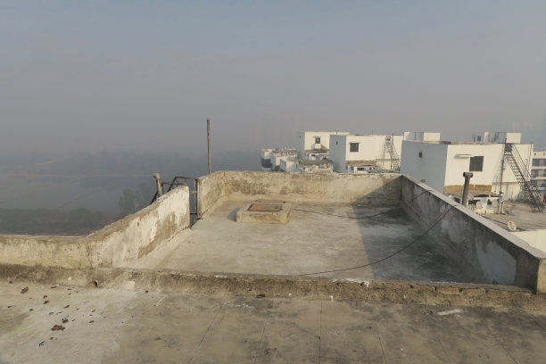 印度北方邦新德里的印度公寓楼屋顶的图片，通过墙上的洞显示早晨雾蒙蒙的天空污染，被污染的雾蒙蒙的天空，德里污染的照片汽车尾气/工厂排放图片下载