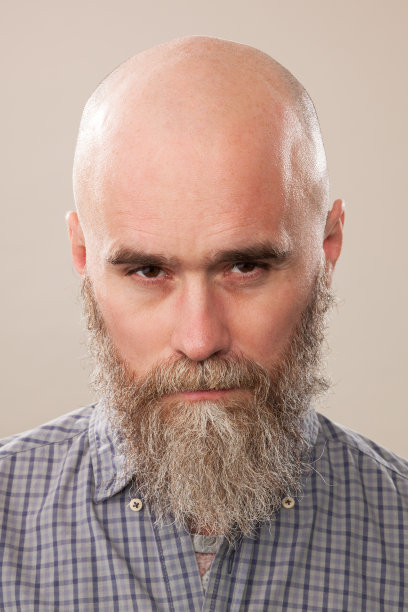 一名40岁剃着光头的大胡子男子的工作室肖像，他穿着一件米色背景的格子衬衫图片下载