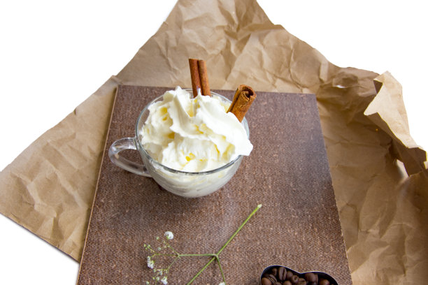 花朵的枝杈，心形的咖啡豆，肉桂棒，玻璃杯里的掼奶油，皱巴巴的包装纸上的棕色调的构图图片下载