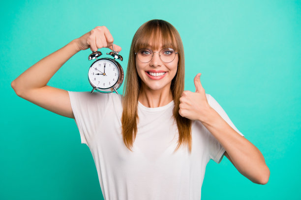 特写照片惊人的美丽，她，她的女士，举起手臂，手，金属闹钟，举起拇指，建议，建议，戴眼镜，休闲的白色t恤，衣服，孤立的蓝绿色背景图片下载