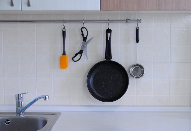 不粘锅，牛排刀，剪刀，金属筛子靠在瓷砖墙上。厨房的内部。图片下载