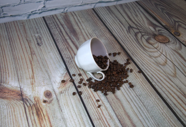 一个瓷杯放在咖啡豆堆里，一张木桌靠在白砖墙上。特写镜头。图片下载