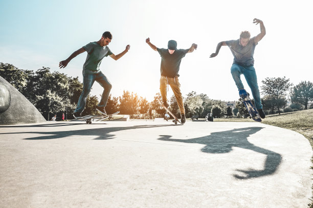 滑板跳跃在城市滑板公园-年轻人表演的技巧和技能在日落在郊区的比赛-极限运动和青年生活方式的概念-主要集中在左边的家伙图片下载