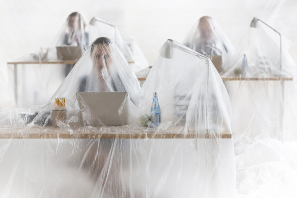 被困在被塑料覆盖的办公桌前使用笔记本电脑的同事图片下载