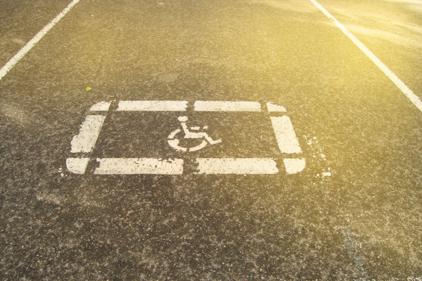 在一个空旷的停车场，阳光下的柏油路上画着残疾人的停车标志图片下载