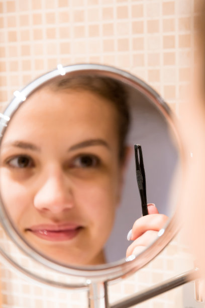 在浴室里照镜子用镊子拔眉毛的美丽女人。美容护肤和健康早晨概念图片下载