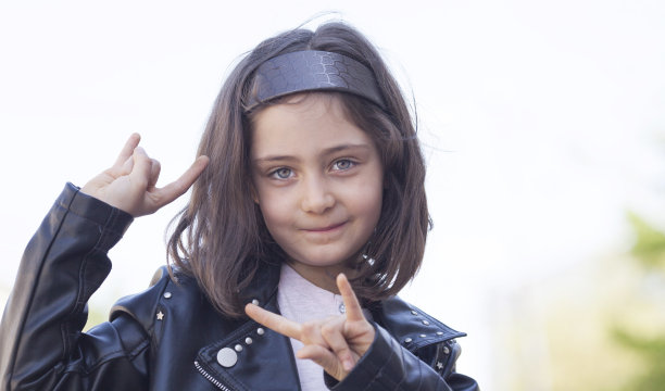 一个穿着摇滚夹克的小女孩做着“那块石头”的手势图片下载